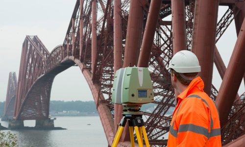 A person in high vis protective wear standing with a piece of scanning equipment overlooking the Forth Rail Bridge.