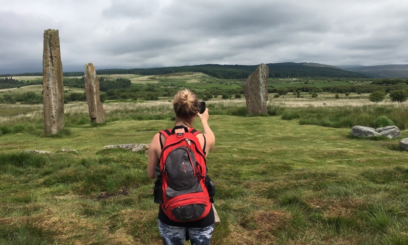A person standing with their back to the camera taking photographs of standing stones
