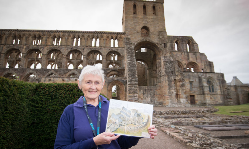 A woman holding a map standing in the grounds of an abbey 