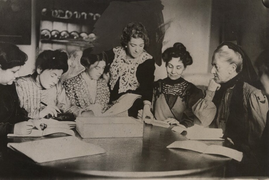A group of women gathered around a table reading papers