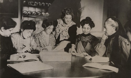 A group of women gathered around a table reading papers