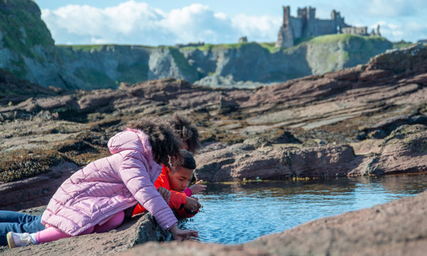 Children playing at a rock pool with Tantallon Castle in the background