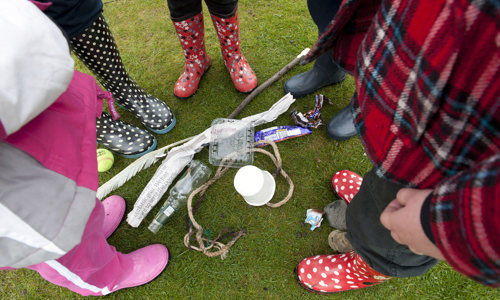 People wearing wellington boots standing in a circle looking down at discarded rubbish on the ground